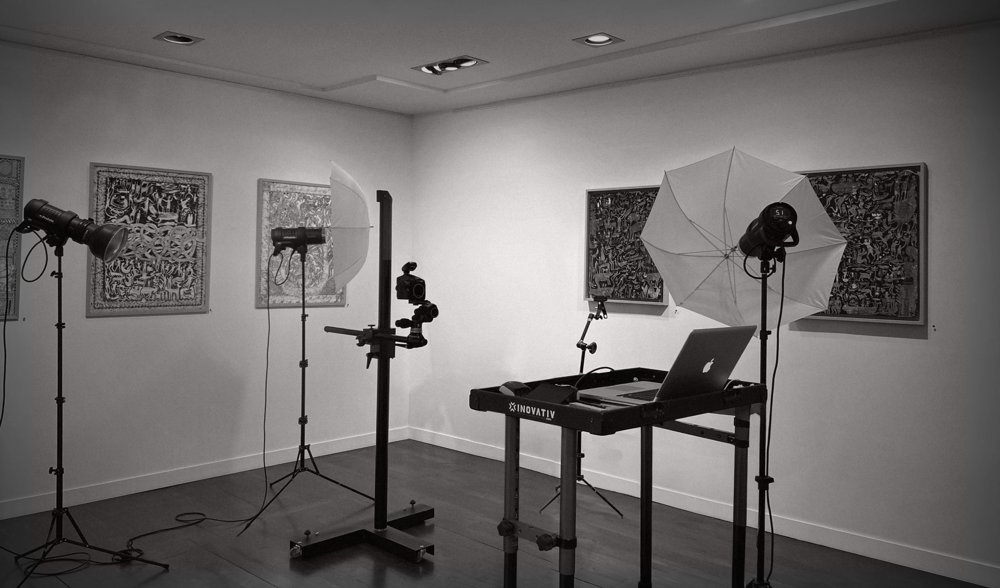Studio de prise de vue installé en galerie : colonne de reproduction, flashs et parapluies devant des tableaux grand format